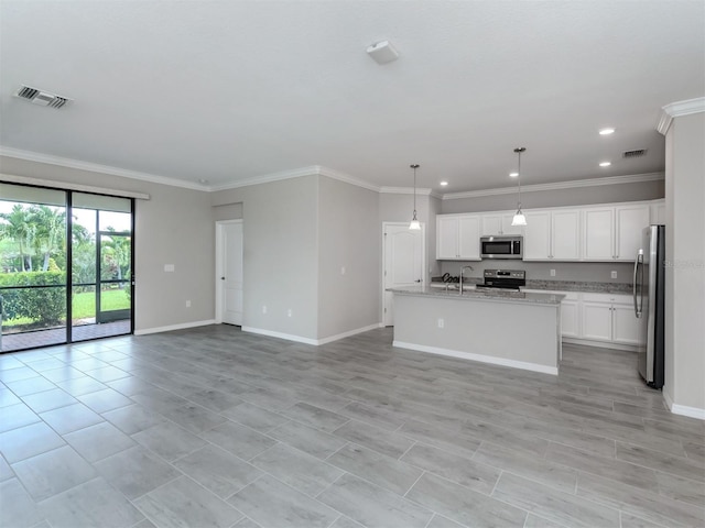 kitchen featuring appliances with stainless steel finishes, an island with sink, white cabinets, hanging light fixtures, and light stone counters