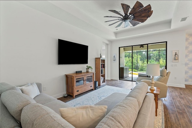 living room featuring ceiling fan, wood-type flooring, and a tray ceiling