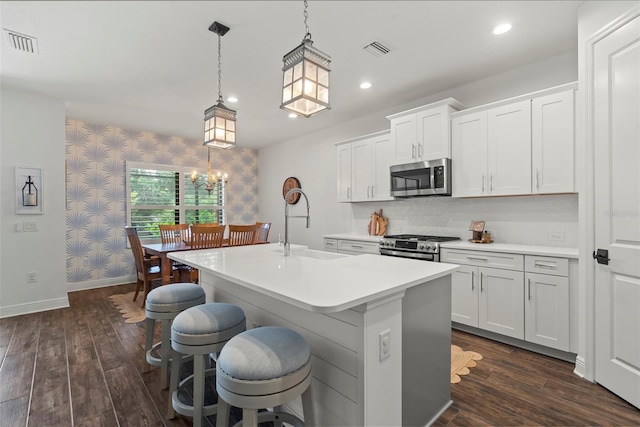 kitchen featuring dark hardwood / wood-style floors, a kitchen island with sink, appliances with stainless steel finishes, sink, and decorative light fixtures