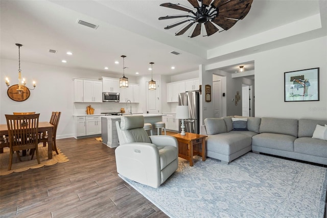 living room featuring an inviting chandelier, a tray ceiling, sink, and hardwood / wood-style flooring