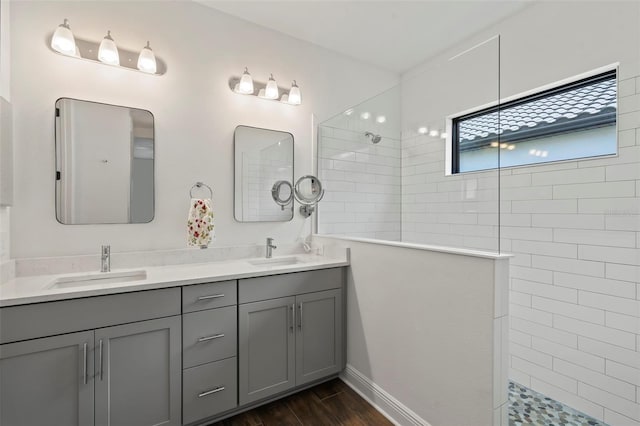 bathroom with wood-type flooring, dual bowl vanity, and tiled shower