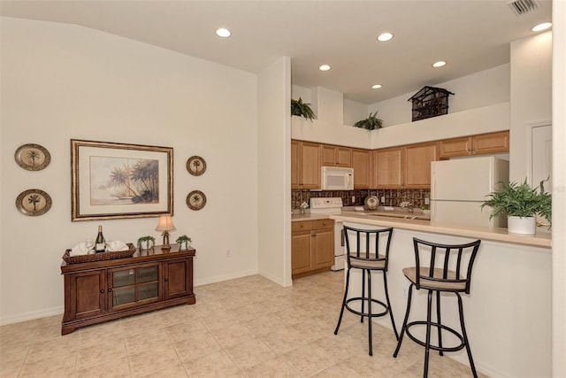 kitchen featuring light tile patterned flooring, backsplash, a breakfast bar area, and white appliances