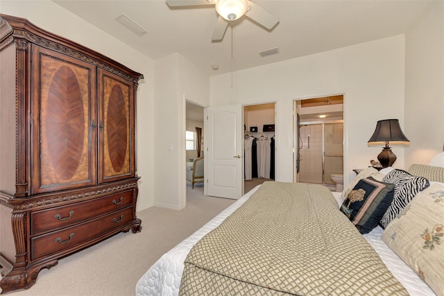 bedroom featuring a walk in closet, a closet, light carpet, ensuite bathroom, and ceiling fan