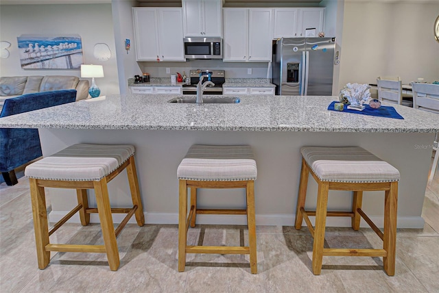 kitchen with a kitchen breakfast bar, appliances with stainless steel finishes, light stone countertops, and white cabinets