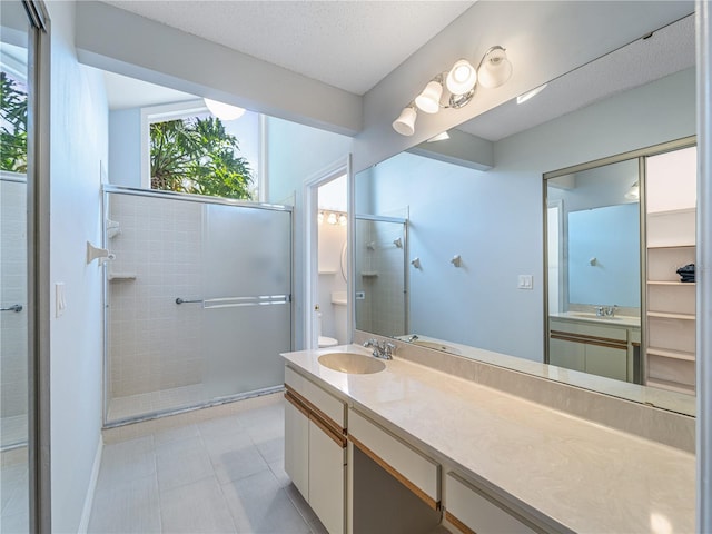 bathroom with a shower with door, a textured ceiling, vanity, and tile patterned floors