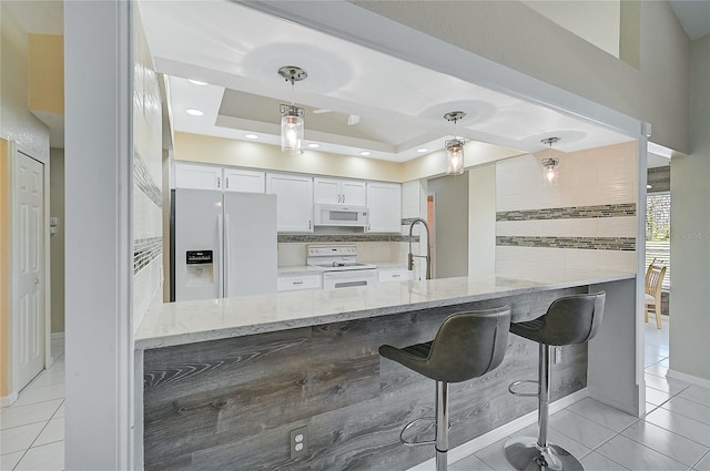 kitchen featuring decorative light fixtures, light stone countertops, white appliances, a tray ceiling, and white cabinets