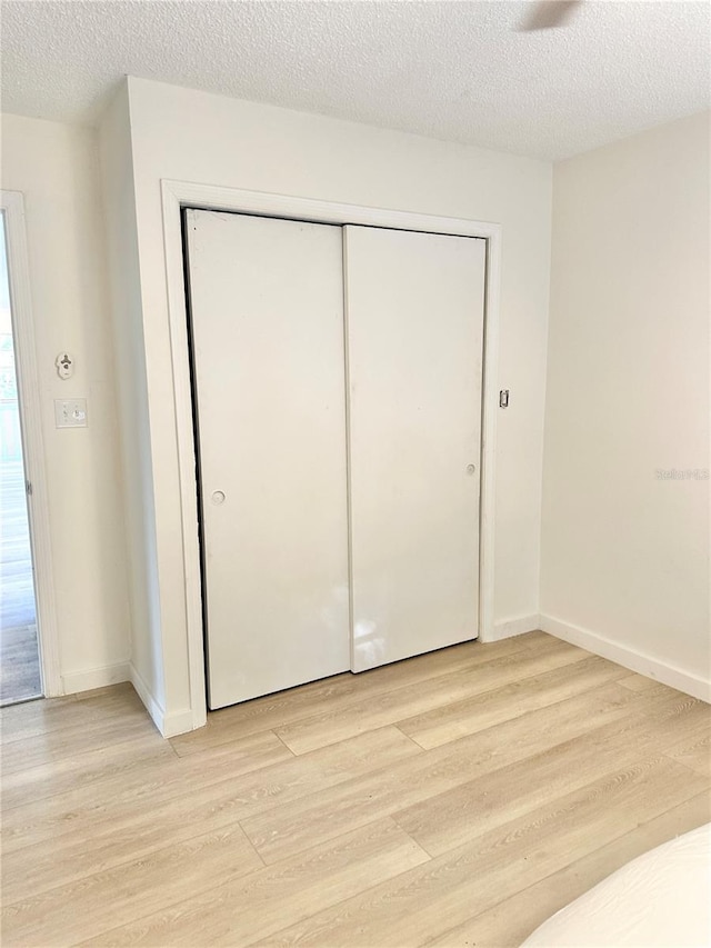 unfurnished bedroom with light wood-type flooring, a textured ceiling, and a closet