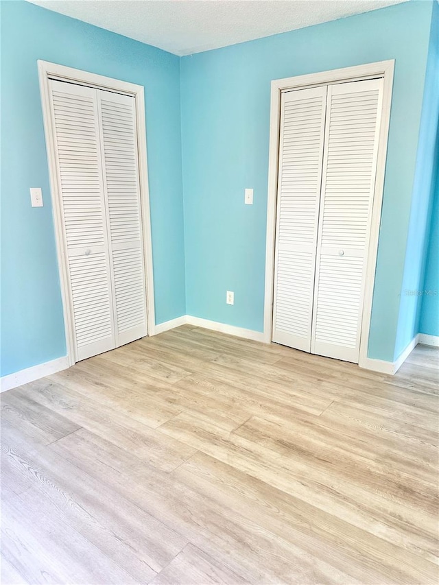 unfurnished bedroom featuring multiple closets and light hardwood / wood-style flooring