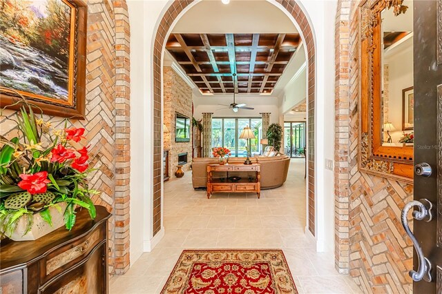 foyer with light tile patterned floors, beamed ceiling, coffered ceiling, ceiling fan, and brick wall