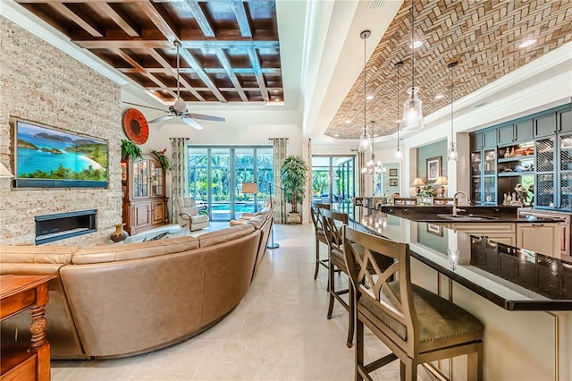 living room featuring sink, a fireplace, ceiling fan with notable chandelier, light tile patterned floors, and a towering ceiling