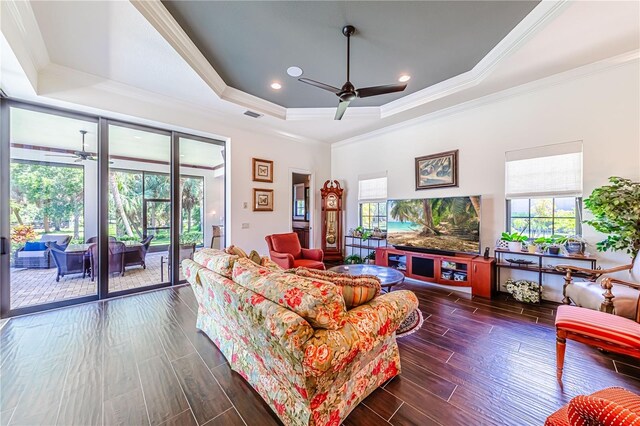 living room with a tray ceiling, ceiling fan, dark wood-type flooring, and ornamental molding