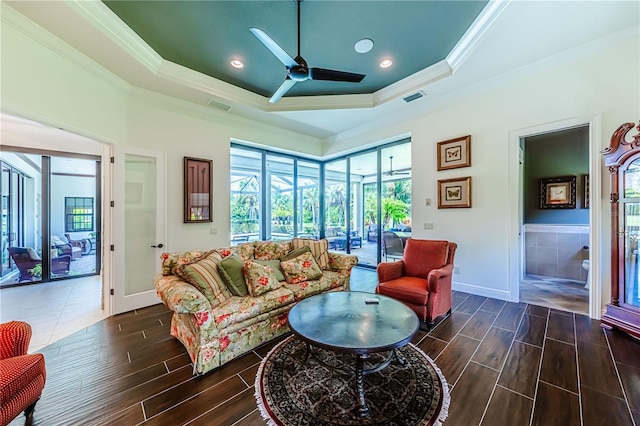 living room with ceiling fan, a tray ceiling, dark wood-type flooring, and ornamental molding