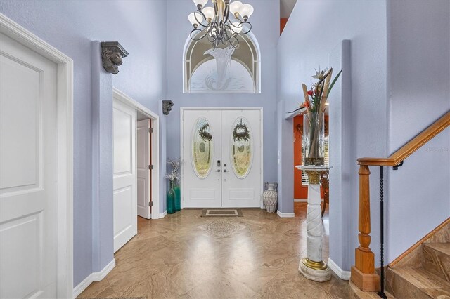 entryway featuring light tile patterned flooring, a chandelier, french doors, and a towering ceiling