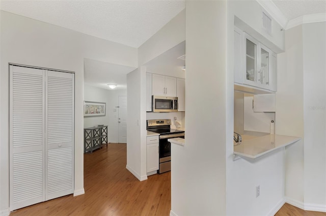 kitchen with a textured ceiling, stainless steel appliances, white cabinets, and light hardwood / wood-style flooring