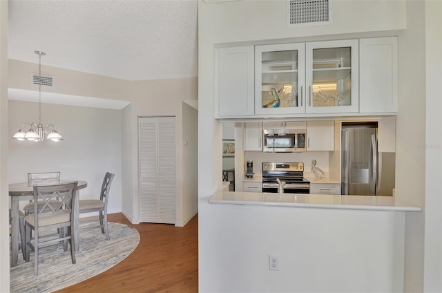 kitchen featuring pendant lighting, hardwood / wood-style floors, white cabinets, appliances with stainless steel finishes, and a notable chandelier