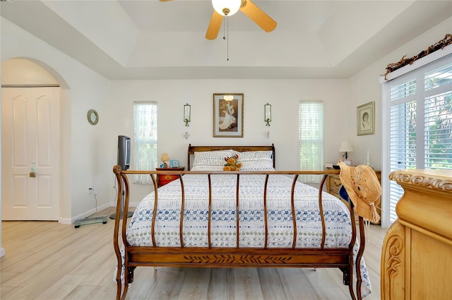 bedroom featuring a raised ceiling, light hardwood / wood-style floors, ceiling fan, and multiple windows