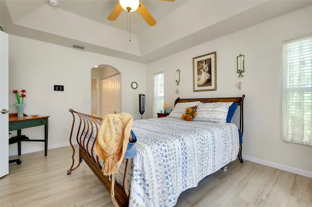 bedroom with light wood-type flooring, a raised ceiling, ceiling fan, and a closet