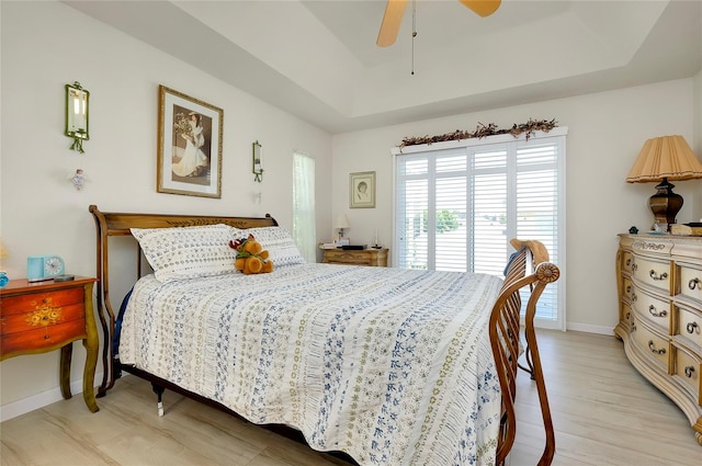 bedroom with ceiling fan, light wood-type flooring, and a tray ceiling