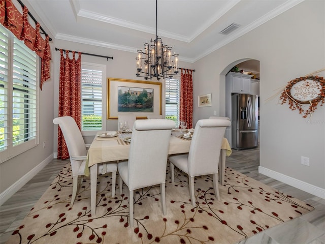 dining room with a tray ceiling, light hardwood / wood-style floors, an inviting chandelier, and ornamental molding