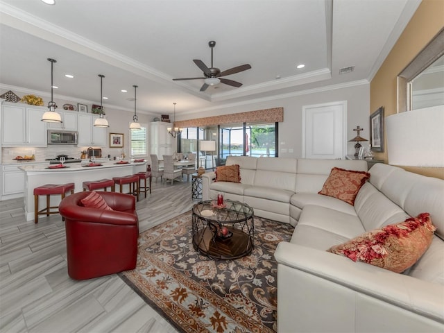 living room with a tray ceiling, ceiling fan, and ornamental molding