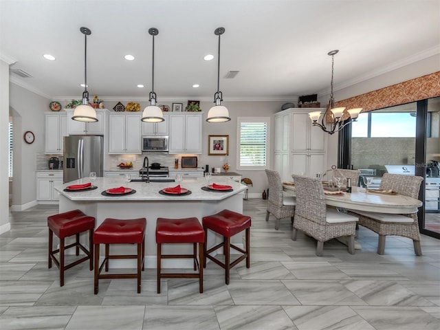 kitchen featuring white cabinets, a breakfast bar area, an island with sink, and stainless steel appliances