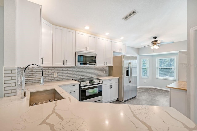 kitchen featuring white cabinets, appliances with stainless steel finishes, light stone countertops, sink, and ceiling fan