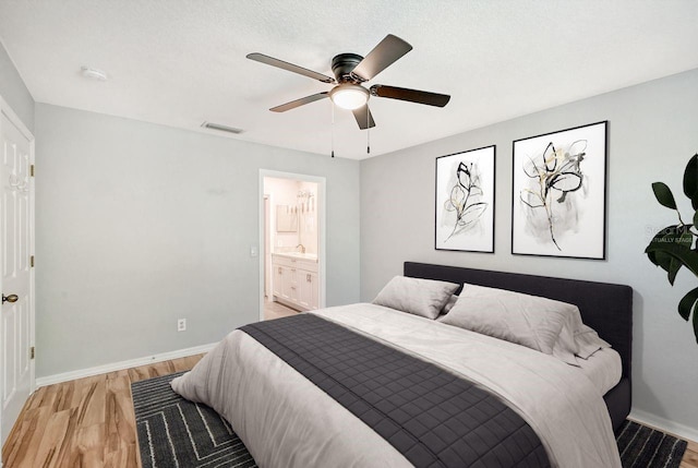 bedroom featuring ensuite bath, a textured ceiling, light hardwood / wood-style flooring, and ceiling fan