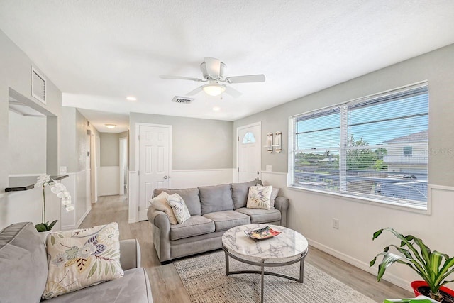 living room with a textured ceiling, ceiling fan, and light hardwood / wood-style floors