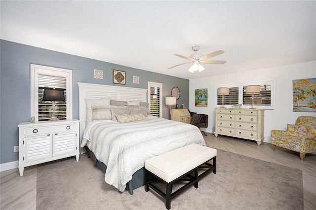 bedroom featuring a ceiling fan, multiple windows, baseboards, and wood finished floors