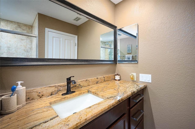 full bath featuring visible vents, a textured wall, tiled shower, and vanity