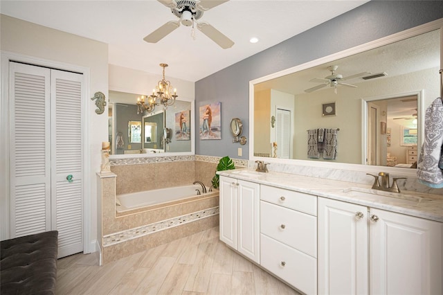 bathroom featuring ceiling fan with notable chandelier, vanity, hardwood / wood-style floors, and tiled tub