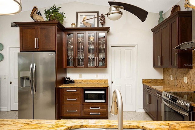 kitchen featuring vaulted ceiling, light tile patterned floors, dark brown cabinetry, light stone countertops, and appliances with stainless steel finishes