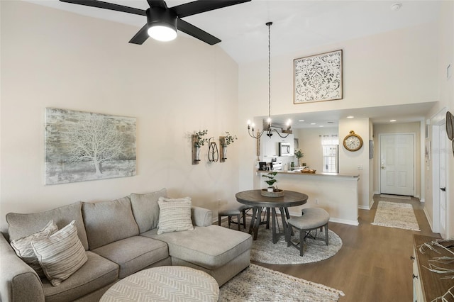 living room with ceiling fan with notable chandelier, hardwood / wood-style flooring, and high vaulted ceiling