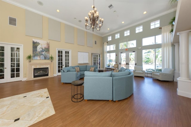 living room featuring a high ceiling, a high end fireplace, french doors, a notable chandelier, and crown molding