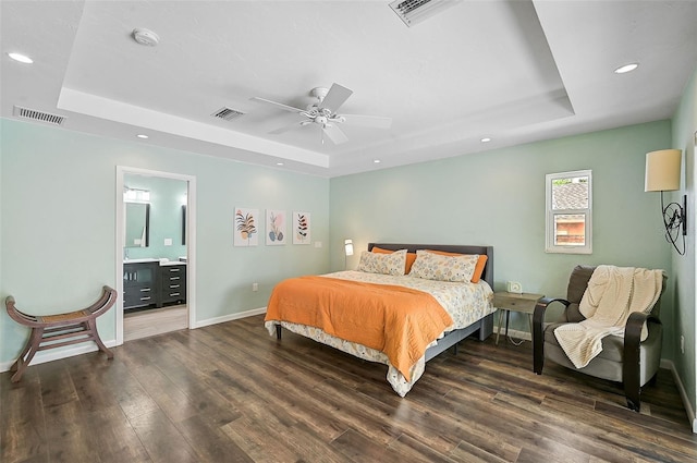 bedroom featuring ceiling fan, ensuite bathroom, a tray ceiling, and wood-type flooring