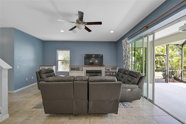 living room featuring ceiling fan, a stone fireplace, and light tile patterned floors