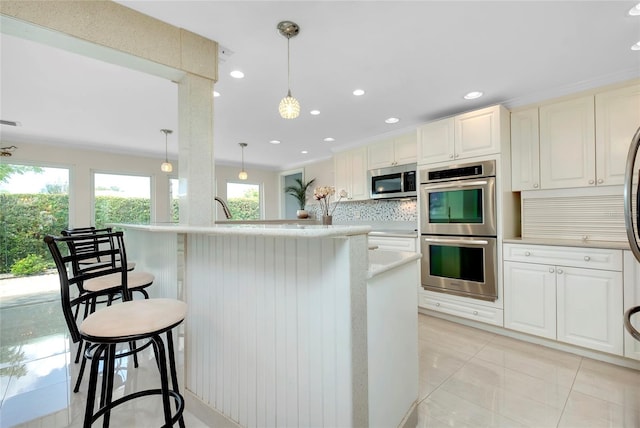 kitchen with light tile patterned floors, a kitchen island with sink, hanging light fixtures, stainless steel appliances, and decorative backsplash