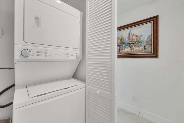 washroom featuring stacked washer / dryer, marble finish floor, baseboards, and laundry area