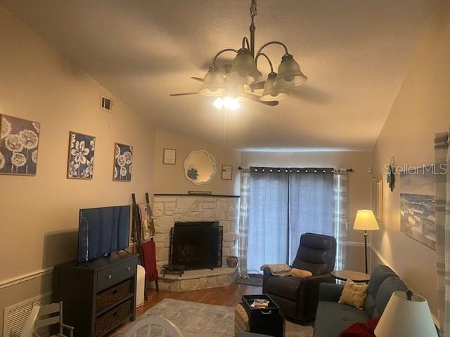 living room featuring ceiling fan with notable chandelier, lofted ceiling, a stone fireplace, and wood-type flooring