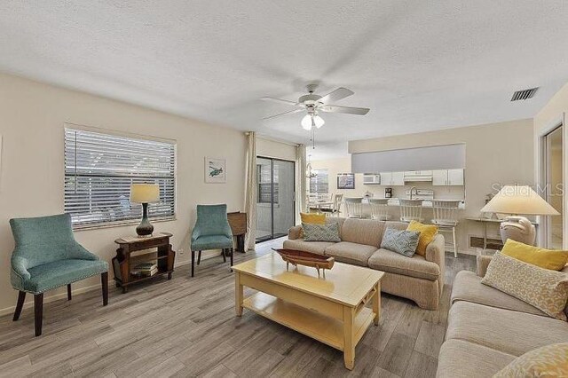 living room featuring ceiling fan, light hardwood / wood-style floors, and a textured ceiling