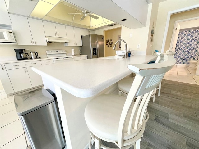 kitchen featuring white appliances, sink, hardwood / wood-style flooring, a kitchen bar, and white cabinetry