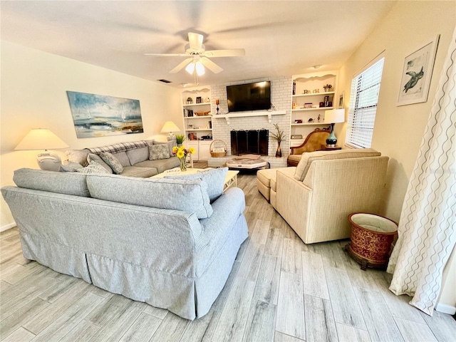 living room featuring ceiling fan, light hardwood / wood-style floors, built in features, and a brick fireplace