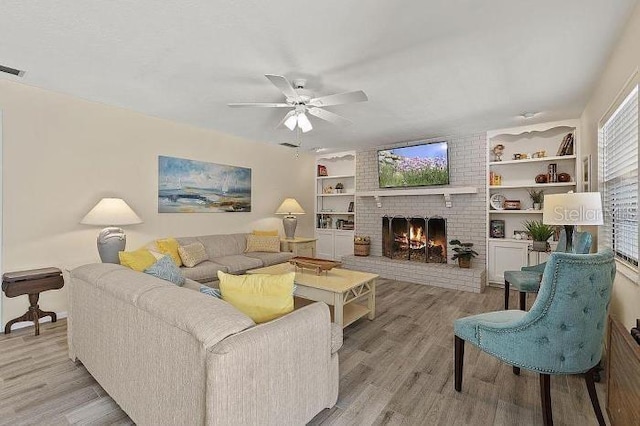 living room with a brick fireplace, ceiling fan, and light hardwood / wood-style flooring