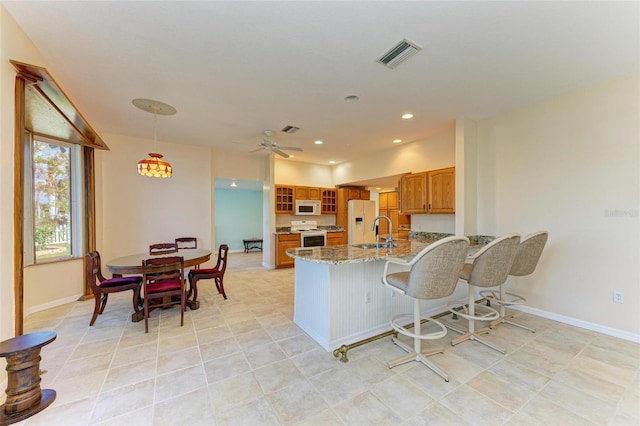 kitchen with white appliances, sink, light stone counters, ceiling fan, and kitchen peninsula