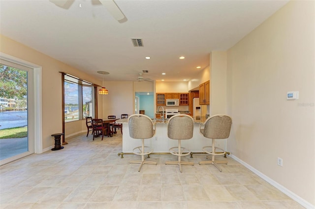 kitchen featuring ceiling fan, white appliances, a kitchen bar, and kitchen peninsula