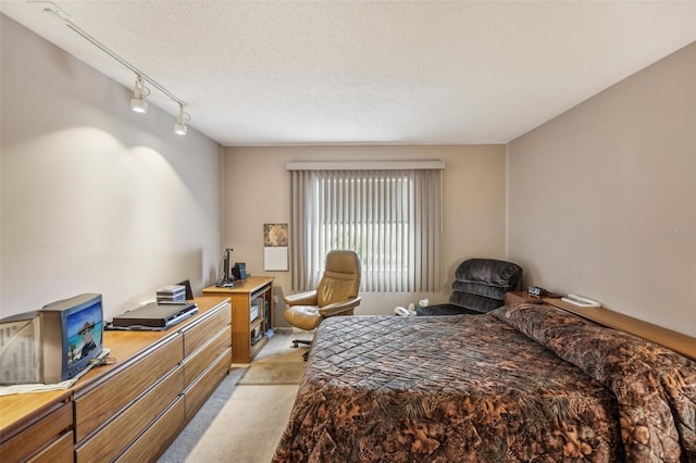 bedroom featuring a textured ceiling, track lighting, and light colored carpet