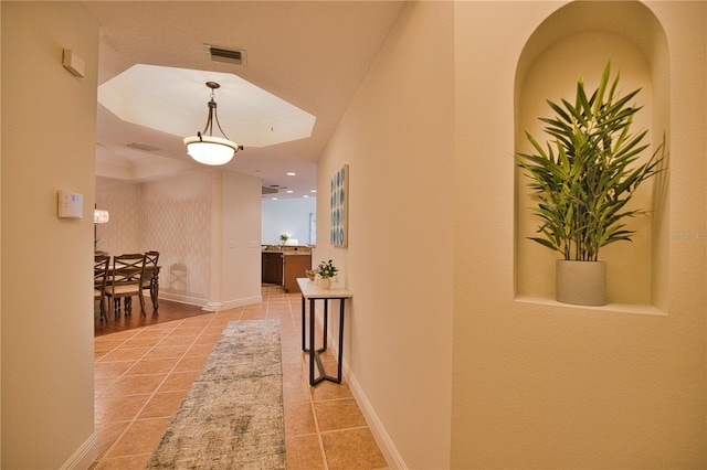 hallway featuring light tile patterned floors, a tray ceiling, visible vents, and baseboards