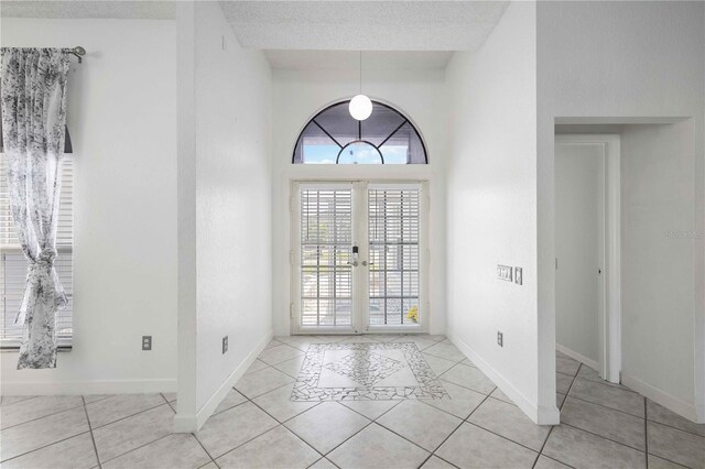 foyer entrance with a textured ceiling, light tile patterned floors, and french doors