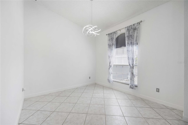 empty room with a textured ceiling, a chandelier, and light tile patterned floors