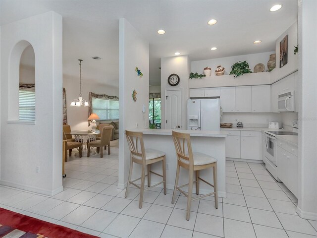 kitchen with white cabinets, white appliances, kitchen peninsula, light tile patterned flooring, and a breakfast bar area